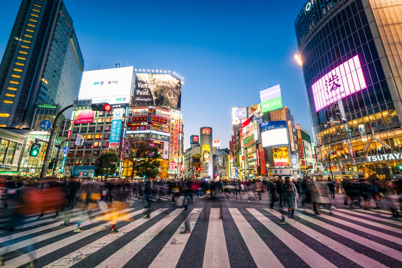 Image of a busy crosswalk in a downtown city in Japan with many buildings and billboards in the background. 