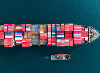 An aerial view of a container ship carrying cargo containers, sailing across the vast ocean.