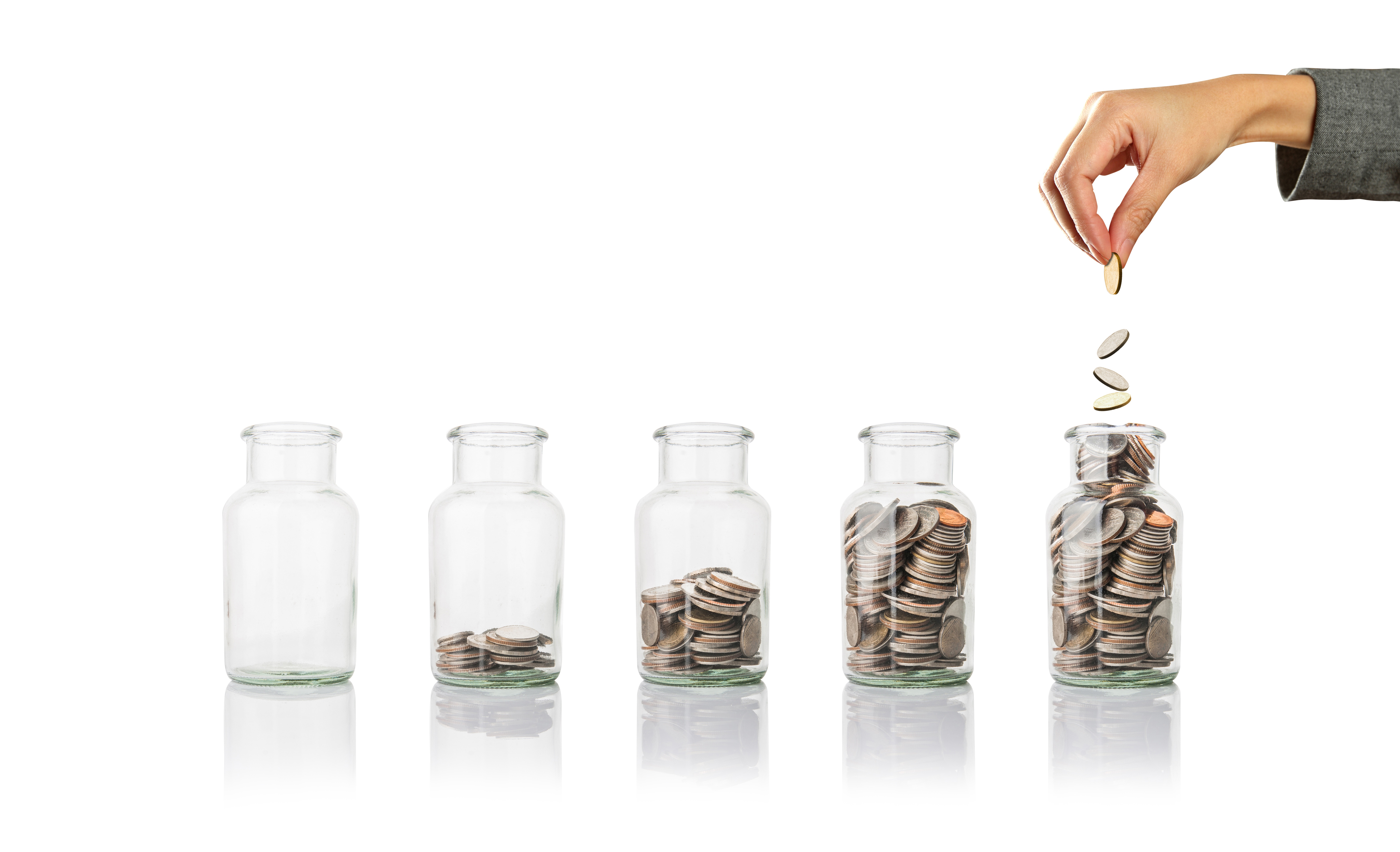 Five jars containing with coins, placed in a row, arranged from the least to the most coins. The first jar is empty. The fifth jar is full with a hand above it dropping more coins into the jar.