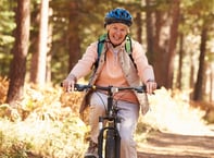 Smiling senior woman mountain biking in the forest