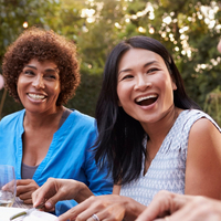 Deux femmes d’âge adulte rient et savourent un repas en plein air.