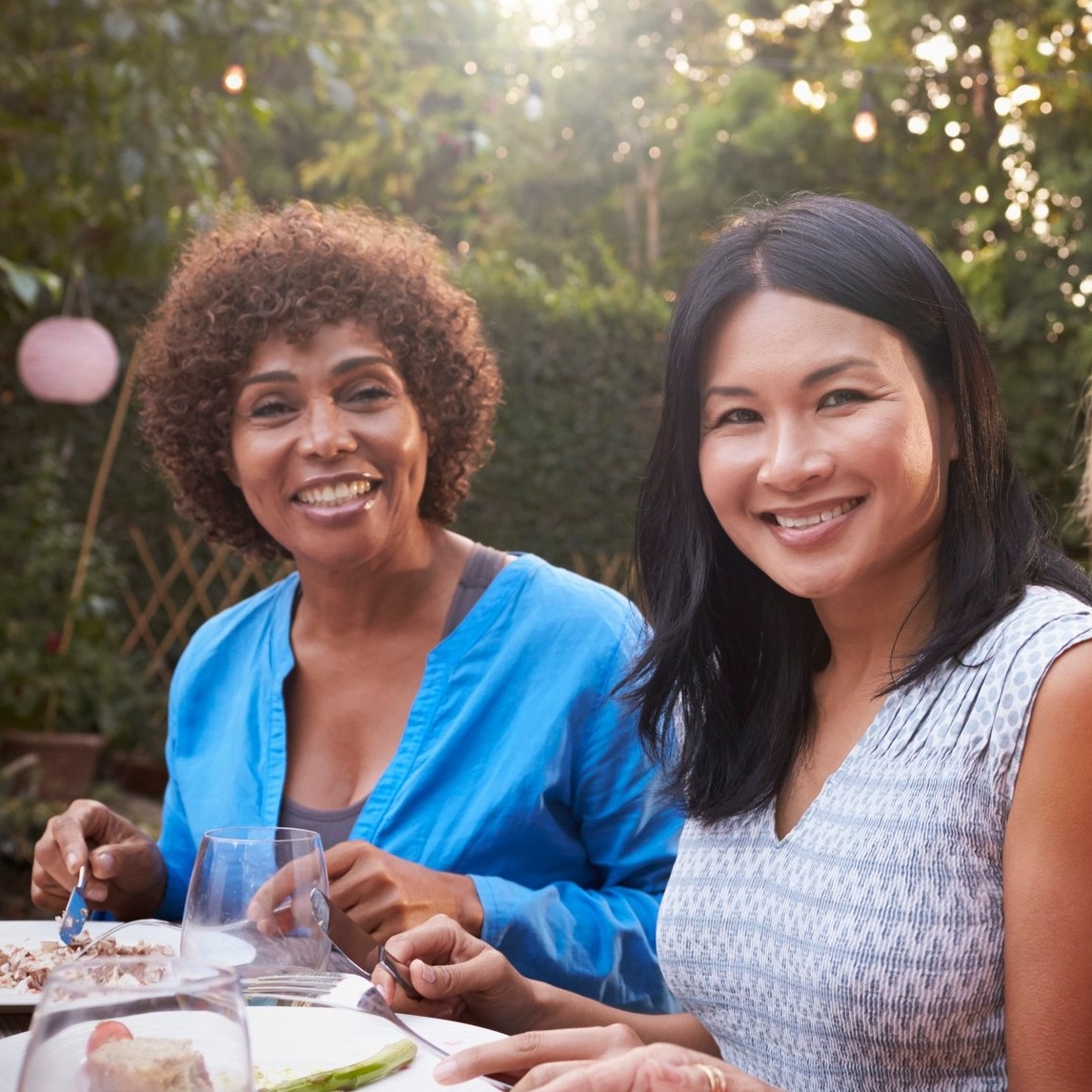 Image de deux femmes d’âge adulte riant et savourant un repas en plein air.
