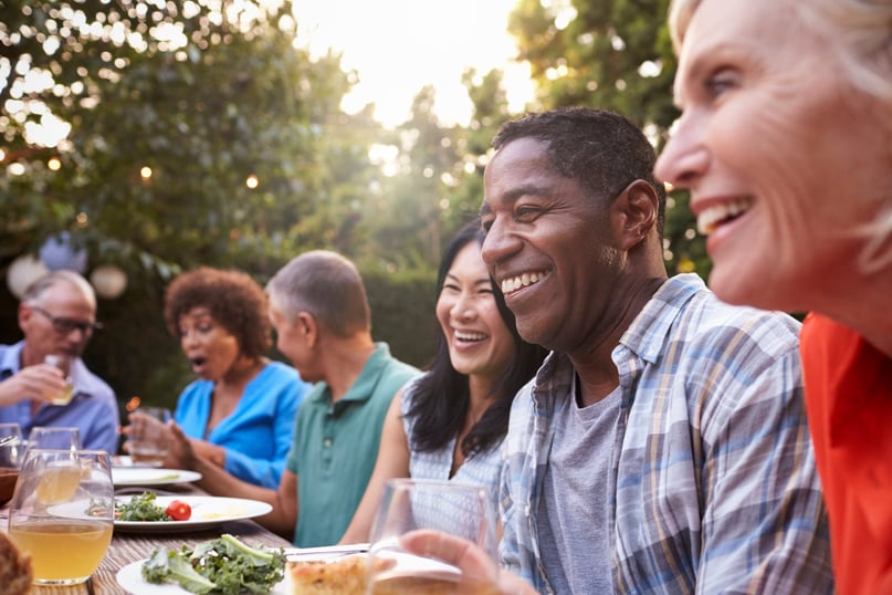 A close-up image of a group of mature family and friends enjoying a meal outdoors in the backyard.
