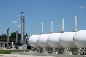 Des réservoirs de stockage de pétrole, et, en arrière-plan, une usine de production de pétrole et d’essence, avec le drapeau des États-Unis hissé au sommet d’une tour de distillation.