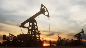 Multiple oil pump jacks working against a dramatic sunset sky.